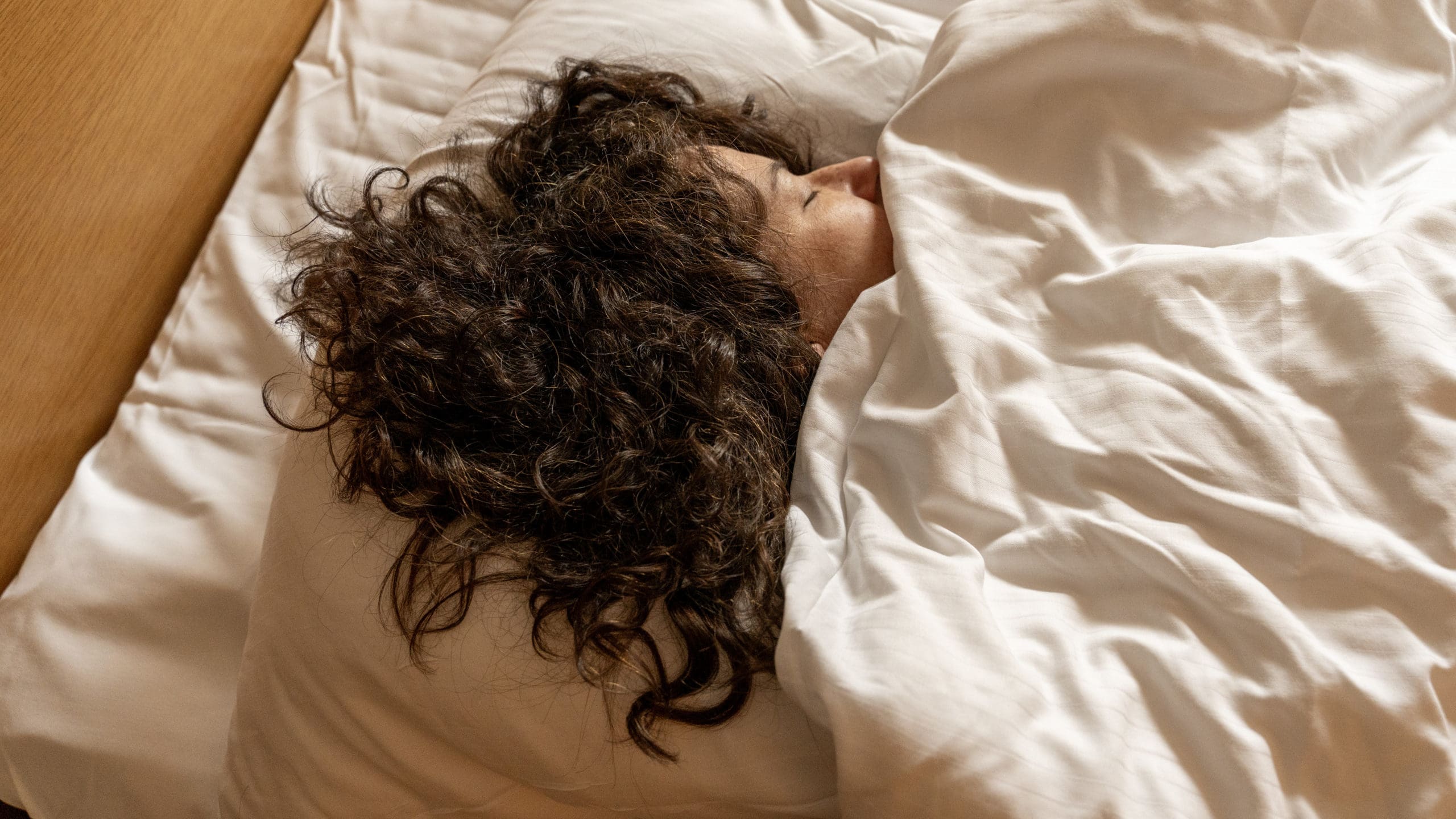 A smiling woman waking up after a relaxing sleep at havila Hotels. She is still laid on the bed with clean and white sheets, and a sunlight coming from the window is warming the atmosphere.