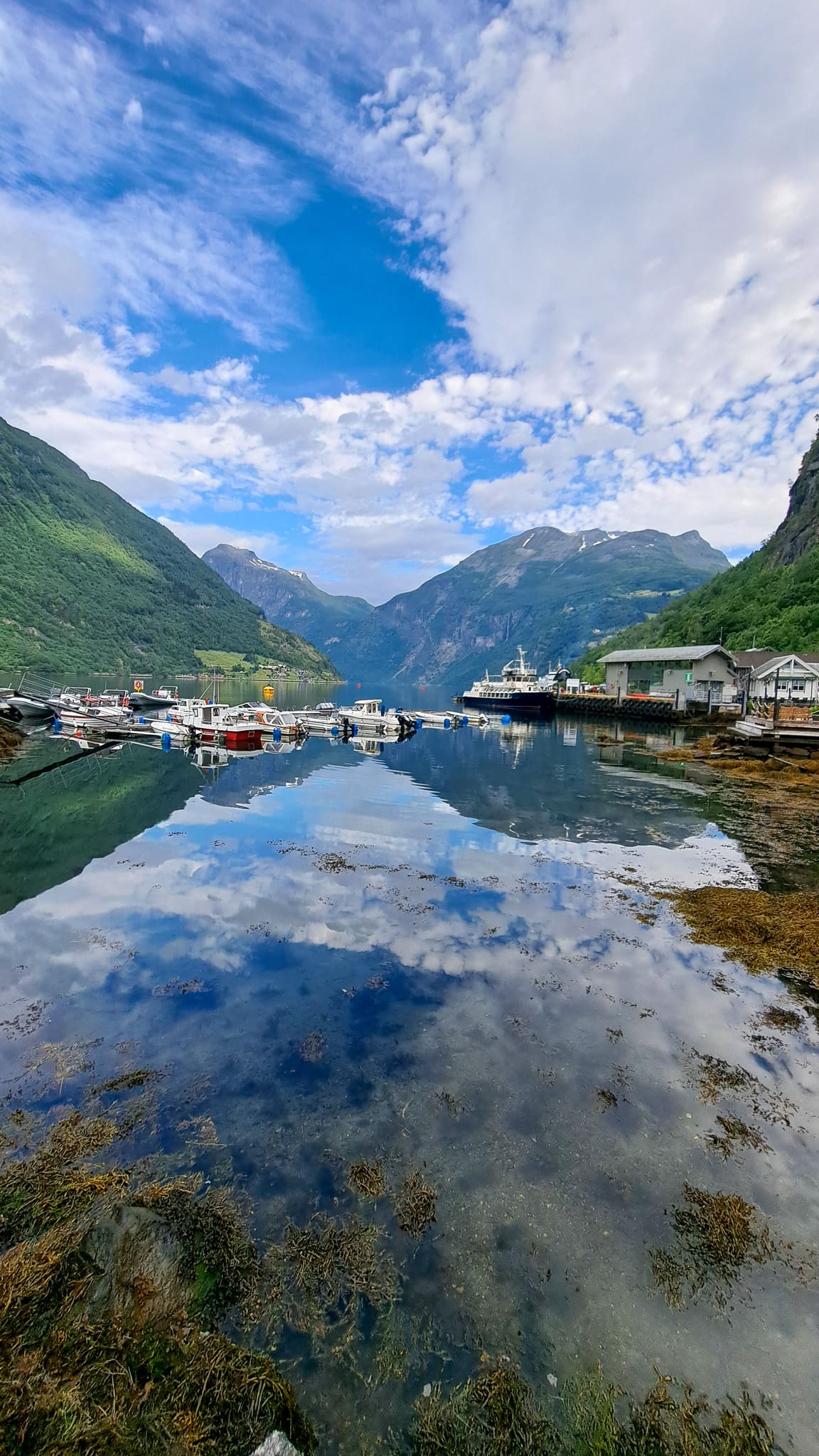 A view of Geirangerfjord from wateredge of Geirangerfjord, just outside Havila hotel Gerianger. The mountains, clouds ski and boats are reflected on the calm water of the fjord.